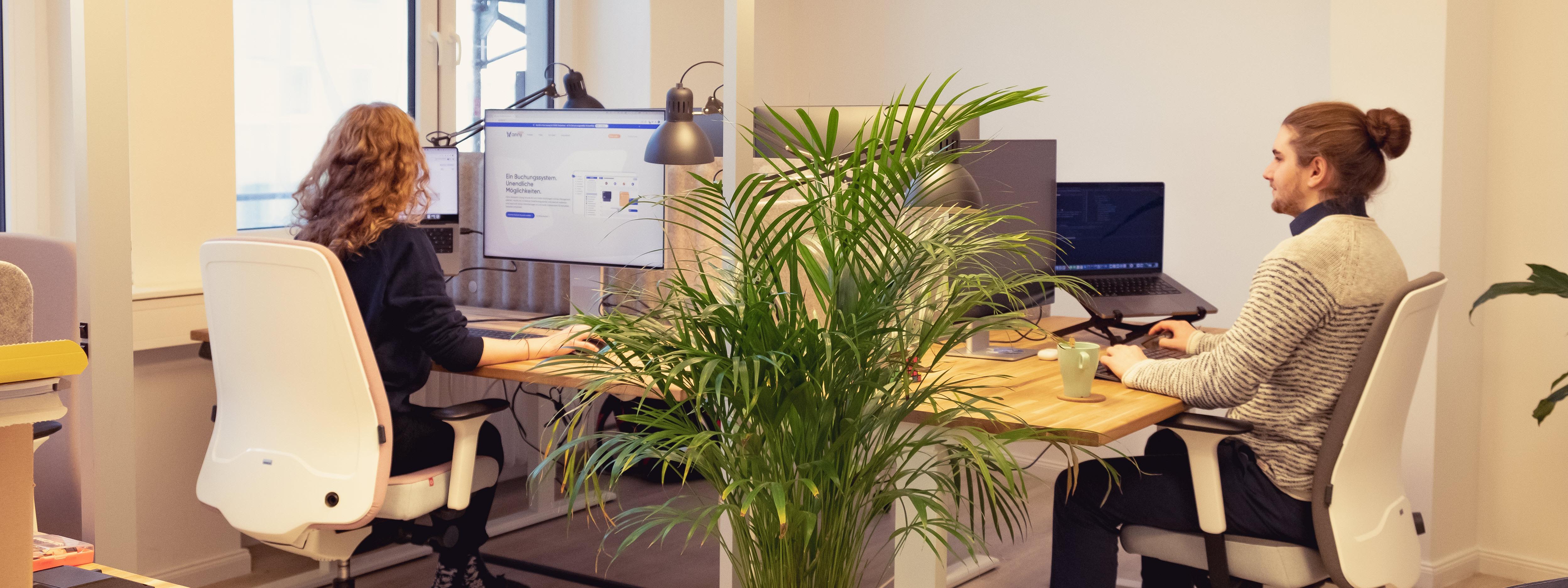 Anna-Carina Jodlauk und Oliver Wycisk sitzen an Schreibtischen im Büro und arbeiten am Computer