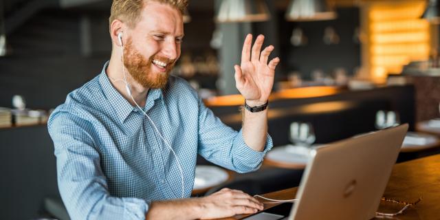 A man sitting in front of a laptop waving his hand