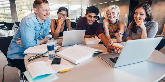 Studierende sitzen um zwei Laptops