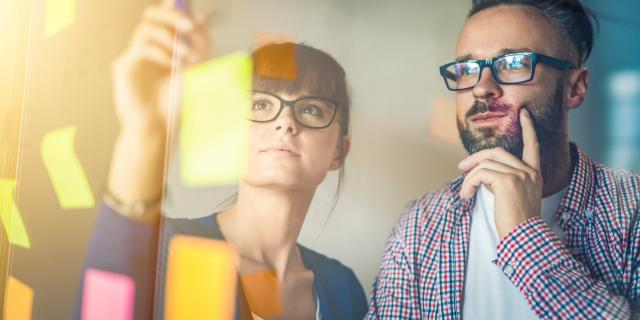 A man and a woman working with post its on a glass wall