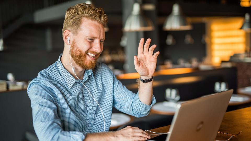 A man sitting in front of a laptop waving his hand