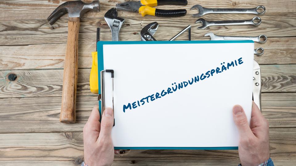 Ein Klemmbrett mit der Aufschrift "Meistergründungsprämie", daneben Handwerkszeug