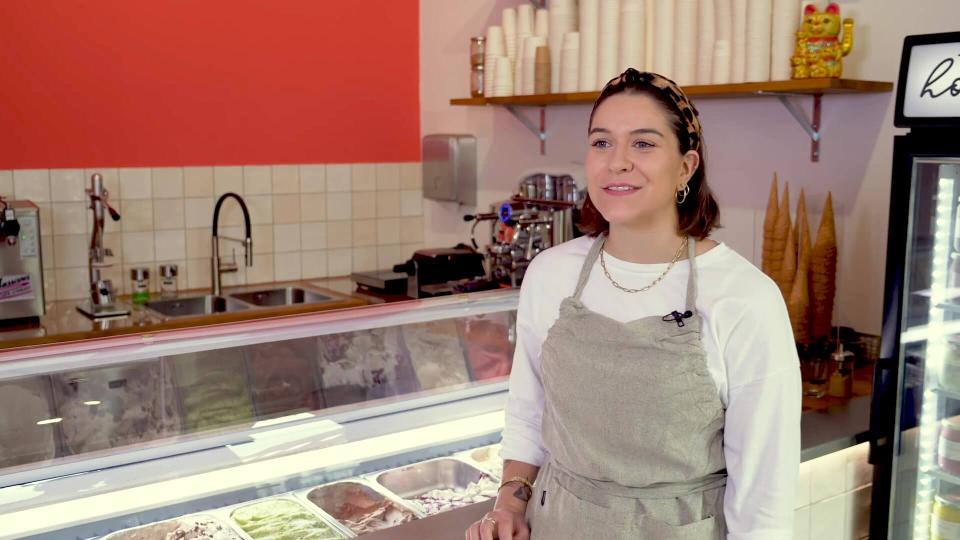 Eine junge Frau, Madeleine Malburg, steht vor dem Tresen einer Eisdiele.