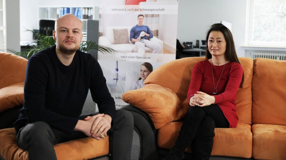 A man with a bald head and a full beard and a woman sitting together on sofas.