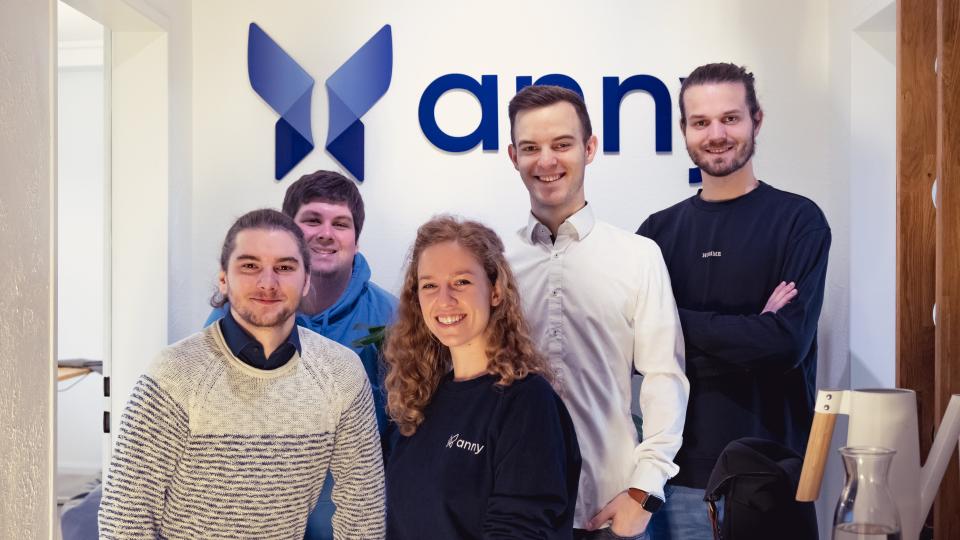 Das Gründungsteam von anny vor dem Firmenlogo an der Wand