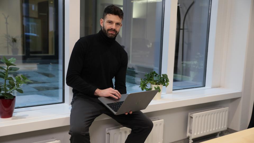 Founder Lukas Haensch is sitting on a window sill with a laptop