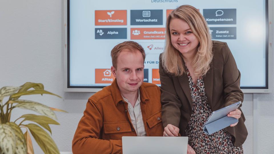 Carolin and Simon Aschemeier in front of a big screen hanging on the wall