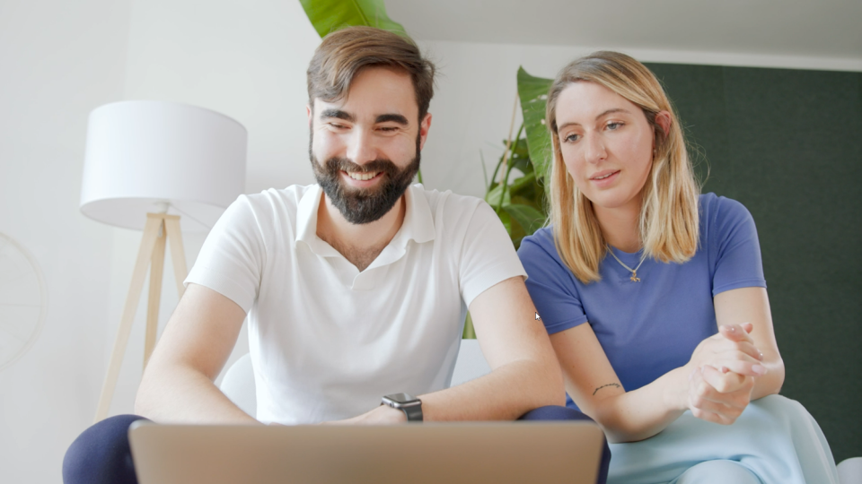 Die Gründenden von Elona Health, Alexander Braden und Johanna von Lobenstein, sitzen auf einem Sofa und schauen auf einen Laptop.