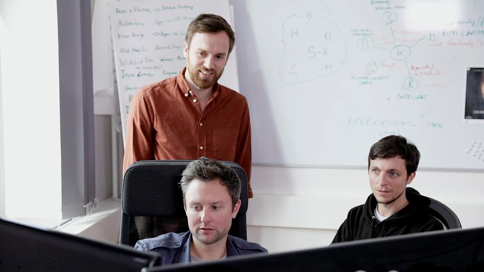 The three founders of Outside the Club in front of two monitors