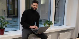 Founder Lukas Haensch is sitting on a window sill with a laptop