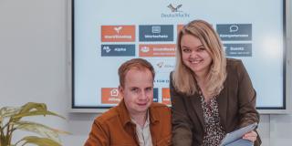 Carolin and Simon Aschemeier in front of a big screen hanging on the wall