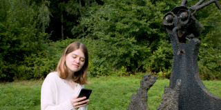 Elisabeth Jacobsohn is standing in a park next to a scalpture looking on her smartphone