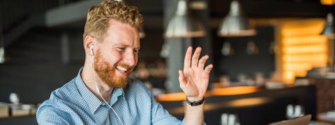 A man sitting in front of a laptop waving his hand