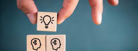 Stacked wooden cubes showing lots of thinking people and a lightbulb on top