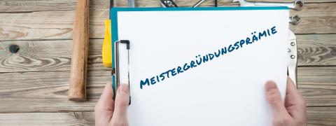 Ein Klemmbrett mit der Aufschrift "Meistergründungsprämie", daneben Handwerkszeug