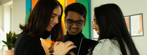 Mona Ghazi, a young female and a young male colleague are looking at a smartphone.