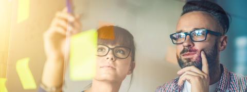 A man and a woman working with post its on a glass wall