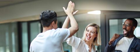 Gruppe junger Leute in einem Büro, ein Mann und eine Frau klatschen sich ab.