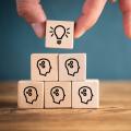 Stacked wooden cubes showing lots of thinking people and a lightbulb on top