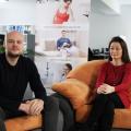 A man with a bald head and a full beard and a woman sitting together on sofas.