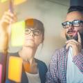 A man and a woman working with post its on a glass wall