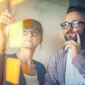 Eine Frau und ein Mann stehen vor einem Glasboard, auf dem Post-its kleben