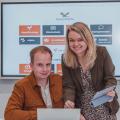 Carolin and Simon Aschemeier in front of a big screen hanging on the wall