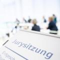 Ein Schild weist auf eine Jurysitzung hin, im Hintergrund sitzt eine Gruppe von Menschen an Tischen