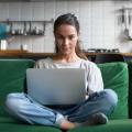 Junge Frau sitzt Laptop im Schneidersitz auf einem Sofa