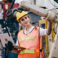 Frau mit Schutzhelm, Warnweste und Laptop prüft den Arm eines Roboters