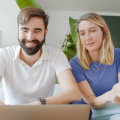 Die Gründenden von Elona Health, Alexander Braden und Johanna von Lobenstein, sitzen auf einem Sofa und schauen auf einen Laptop.