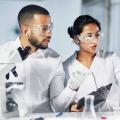 Mann und Frau mit Schutzbrillen stehen vor einem Computerbildschirm in einem Labor