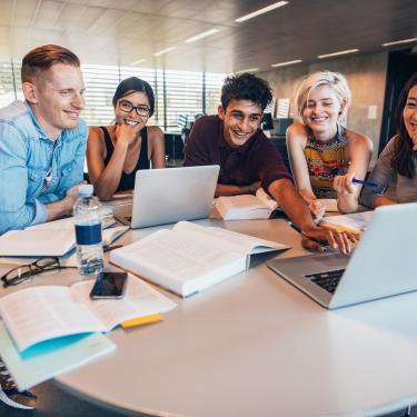 Studierende sitzen um zwei Laptops